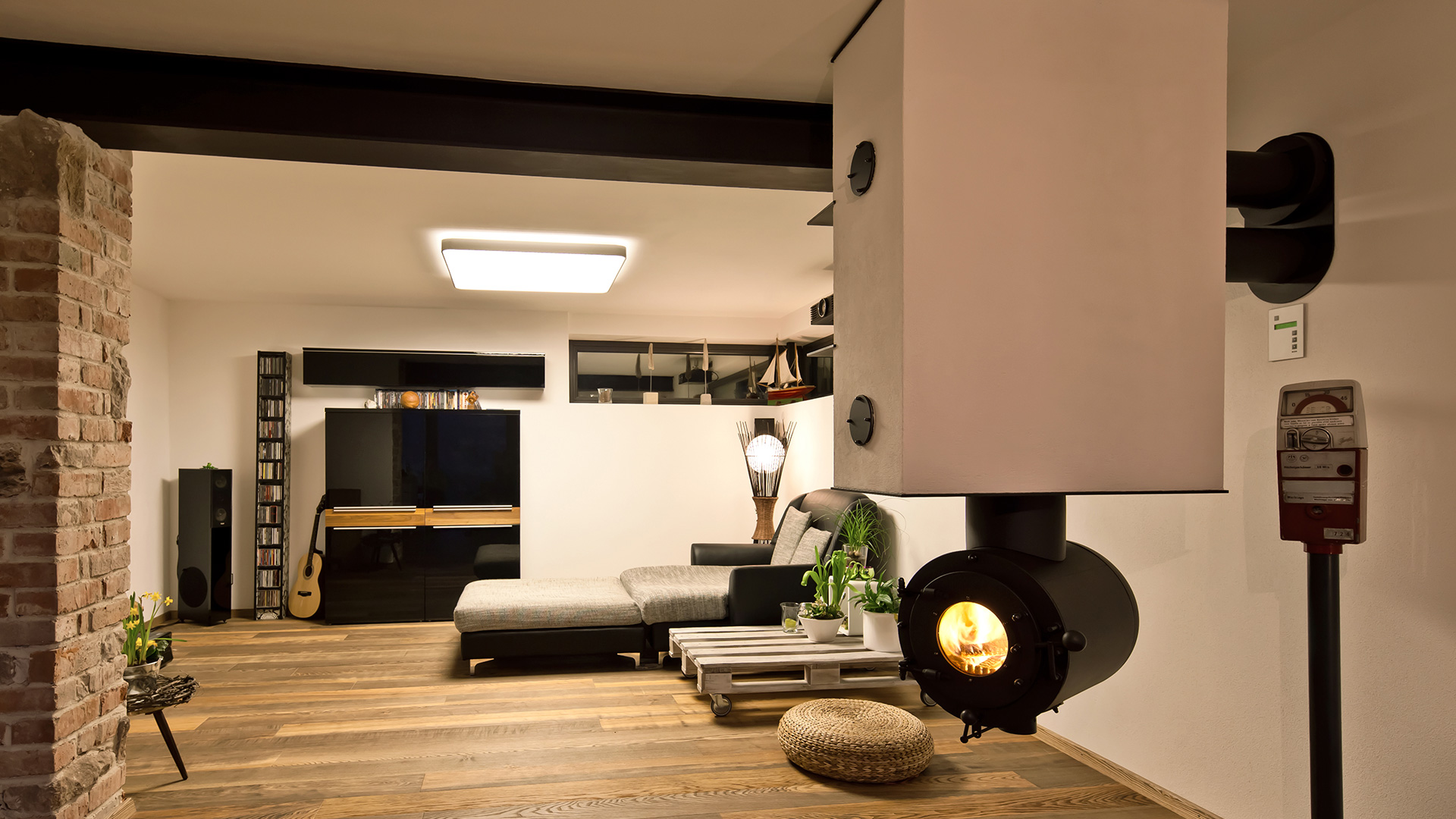 Modernes Wohnzimmer mit von der Decke hängendem schwarzen firetube Ofen und sichtbarem Feuer; im Hintergrund Möbel.