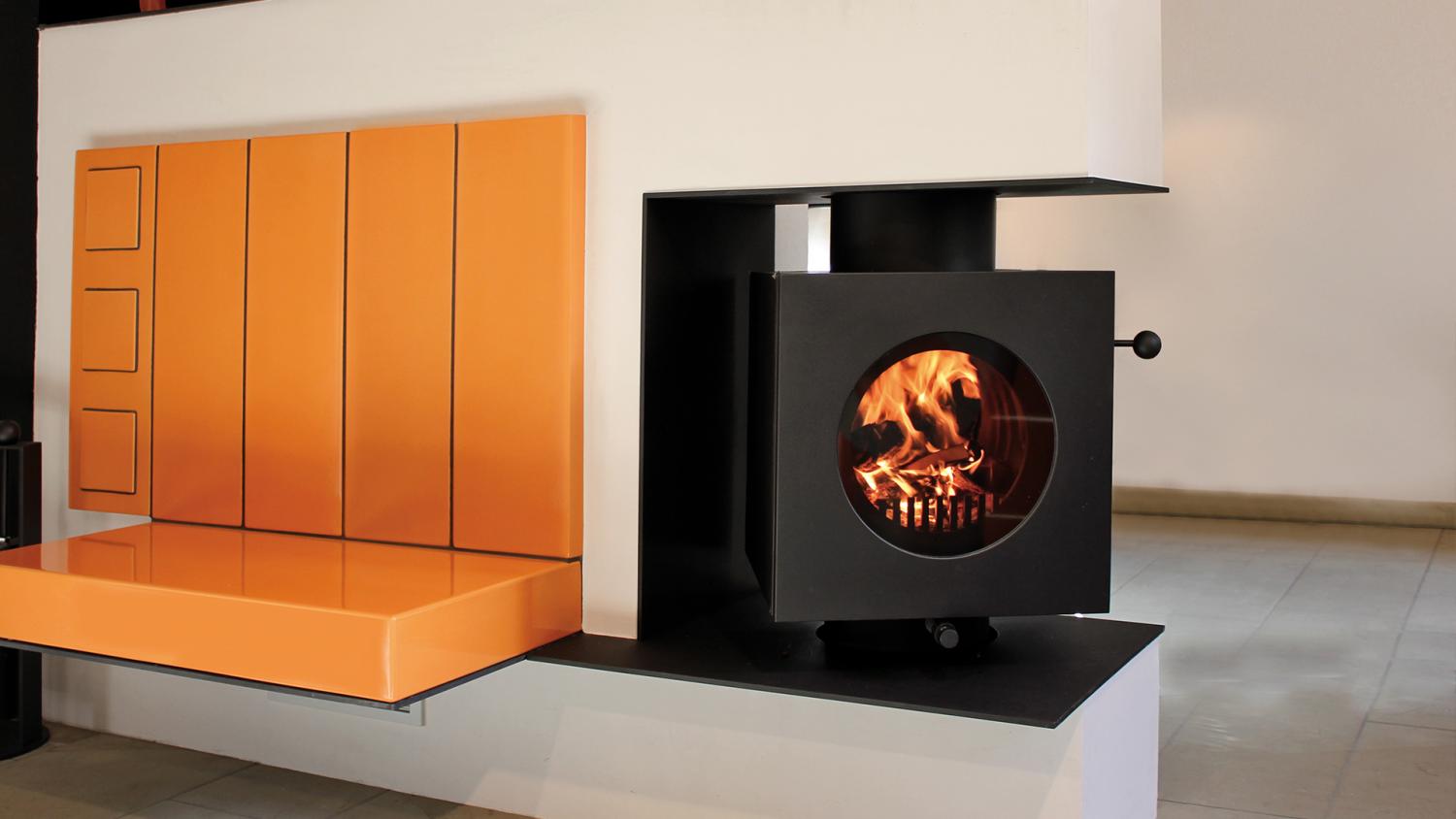 Schwarzer rechteckiger firetube Ofen mit sichtbarem Feuer, integriert in eine trennende Wohnwand; links daneben eine Sitzfläche.