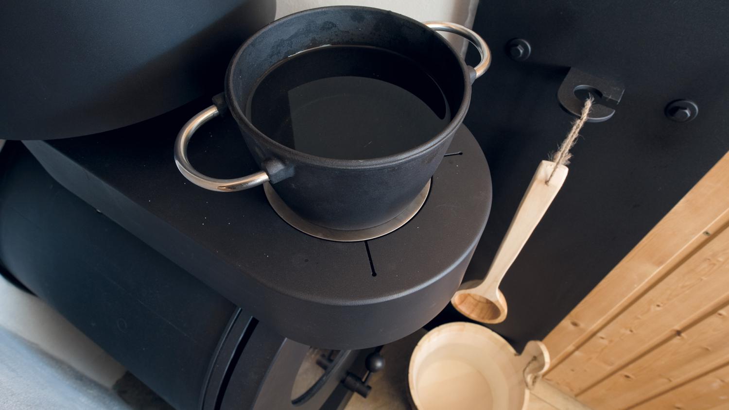 Hotplate eines firetube Ofens mit Topf mit Wasser darauf; daneben ein Holzlöffel und ein Holzeimer.