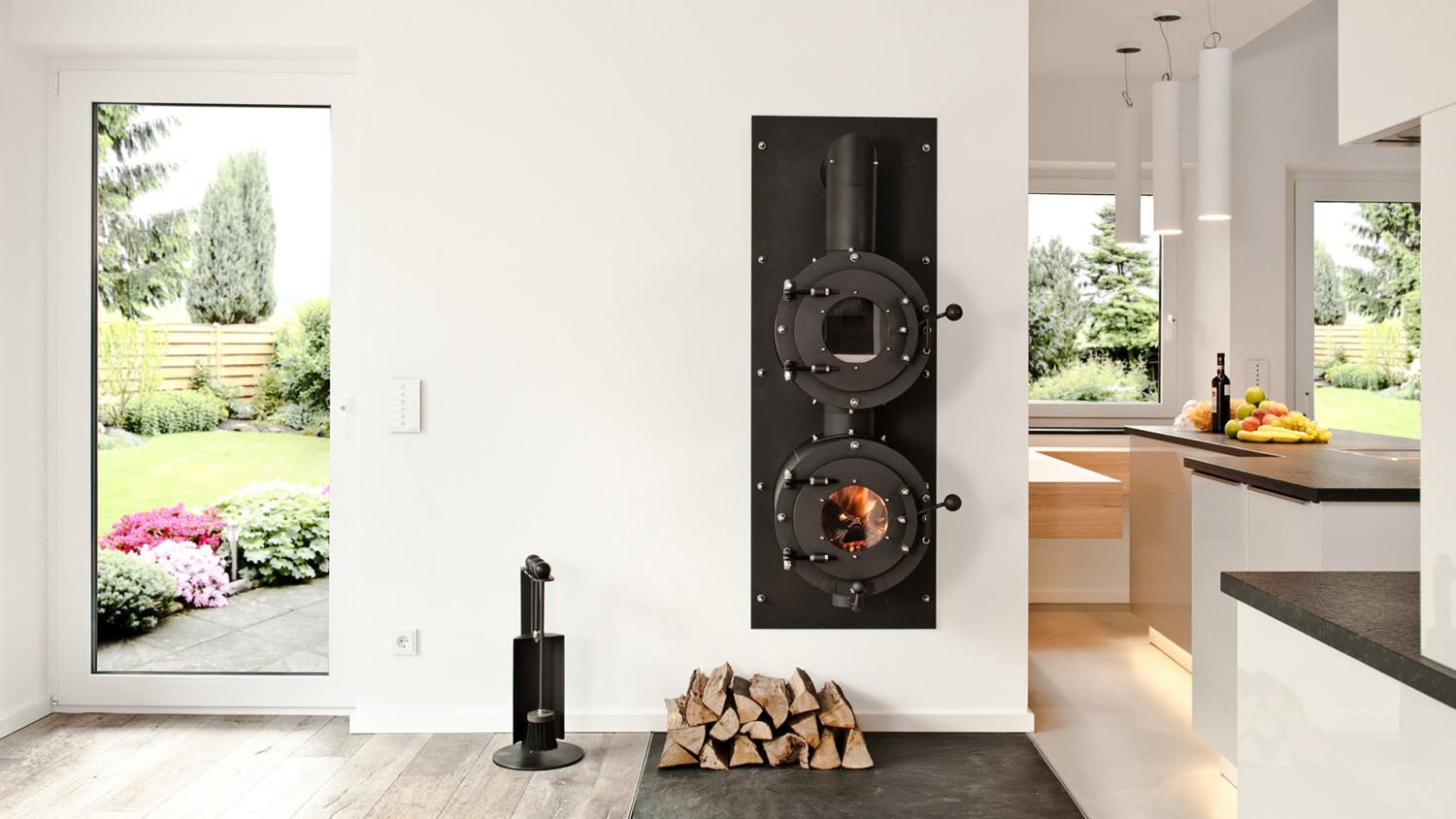 Firetube Ofen mit Garraum darüber, in eine Wohnwand integriert; darunter Holzscheite; rechts Küche, links Terrassentür.