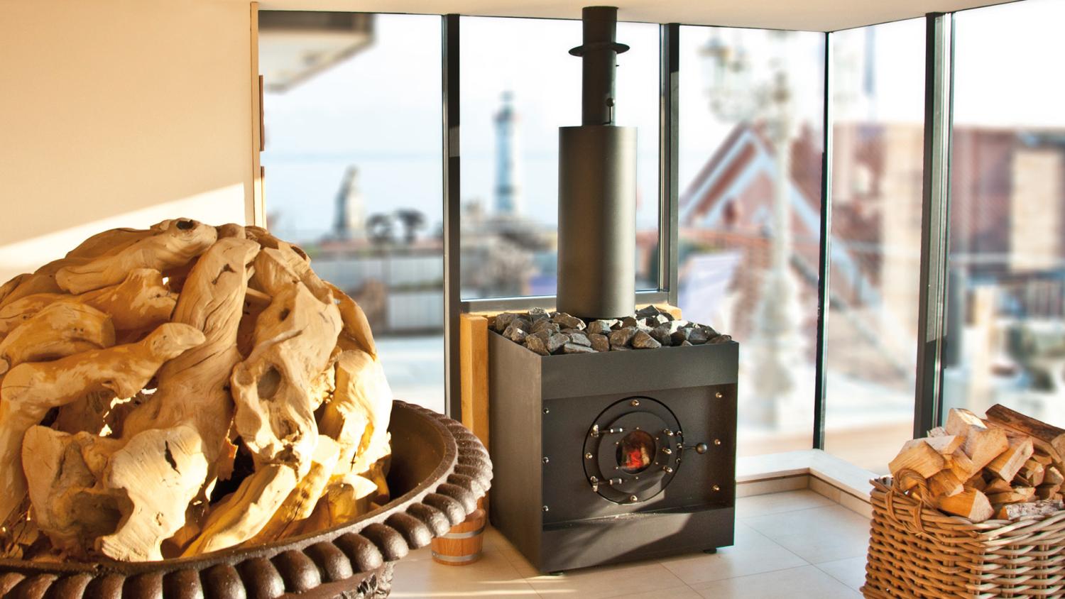 firetube Saunaofen in Sauna mit Glaswand, davor Holzdekoration und Korb mit Holzscheiten auf dem Boden.