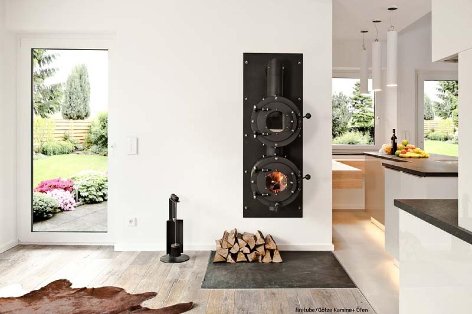 Firetube Ofen mit Garraum darüber, in eine Wohnwand integriert; darunter Holzscheite; rechts Küche, links Terrassentür.