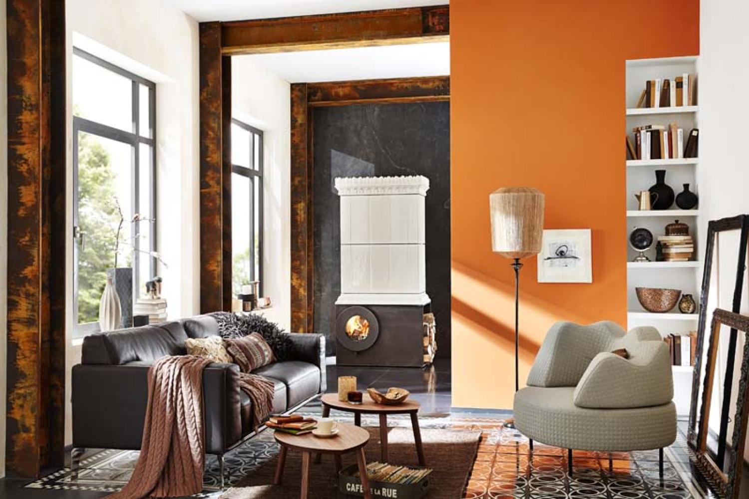 Schwarzer firetube Ofen mit sichtbarem Feuer und Säulenkonstruktion darüber, in wohnlicher Umgebung mit Sofa, Tischen und Stühlen.