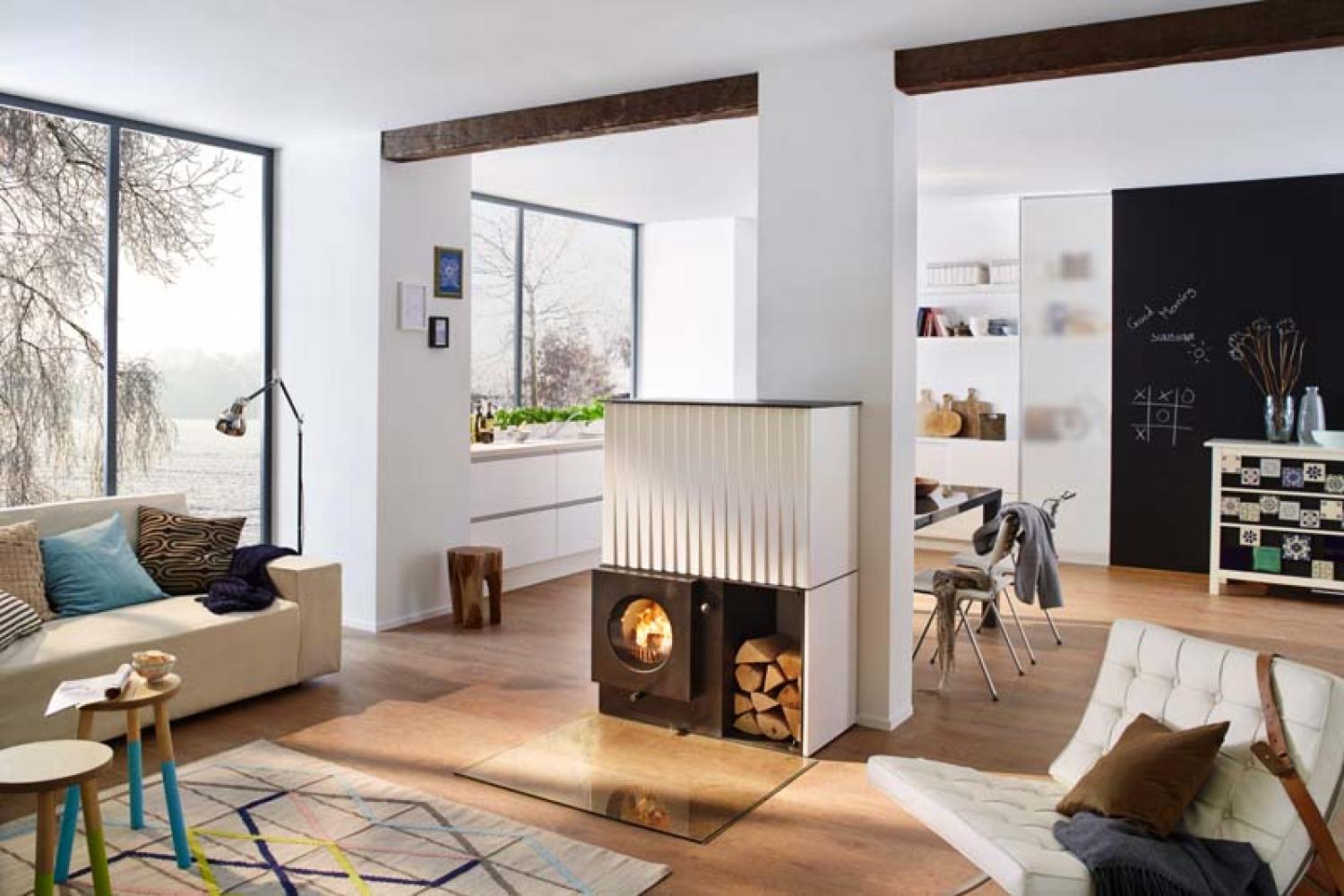 Wohnzimmer mit schwarzem firetube Ofen und sichtbarem Feuer; daneben gestapelte Holzscheite, umgeben von Möbeln und Fenstern.