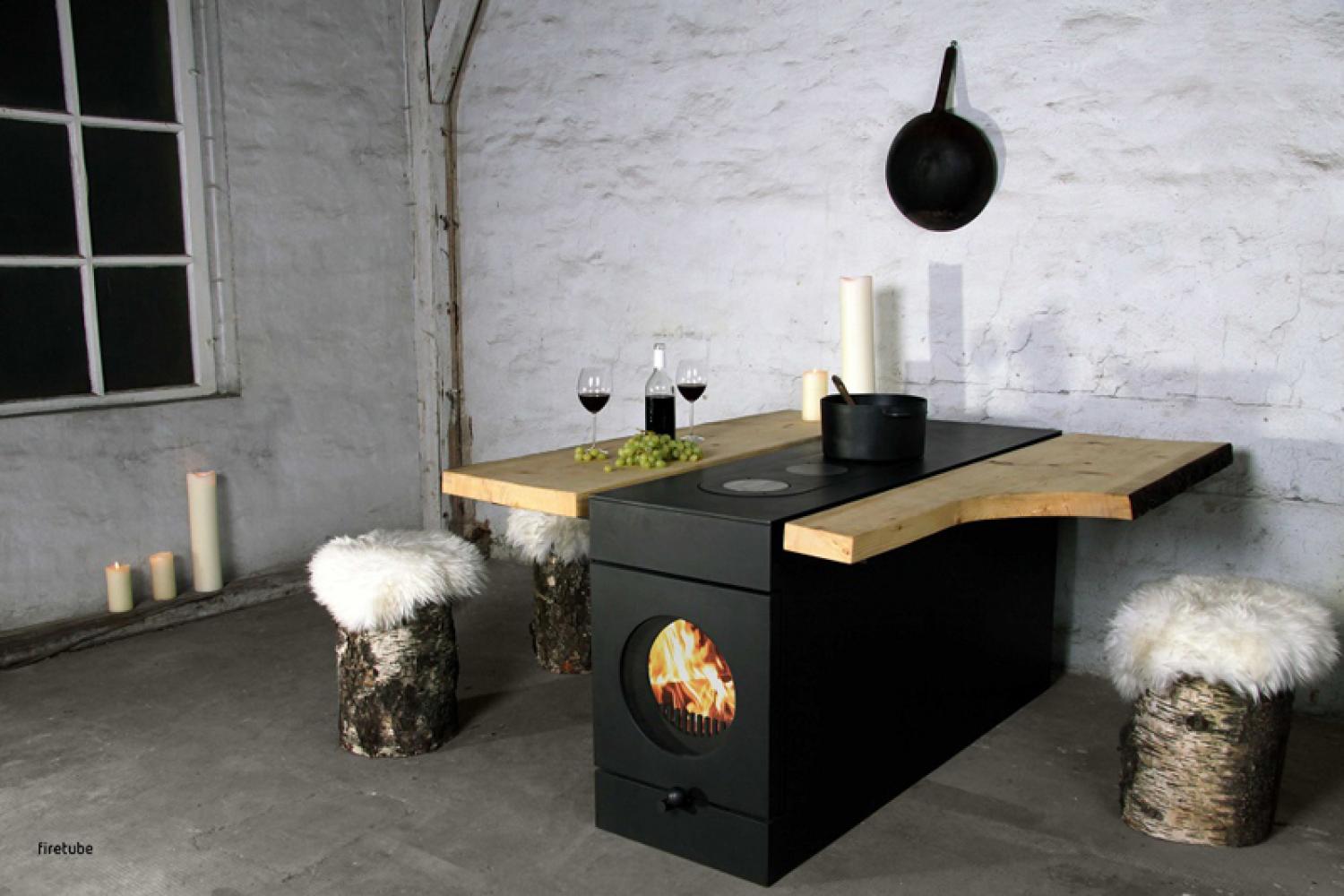 firetube Ofen mit sichtbarem Feuer, integriert in eine Küchenzeile mit Wärmeplatten und Topf; Holzverlängerung mit Weingläsern, Trauben und Kerzen, rustikales Ambiente mit Holzhockern und Fell.