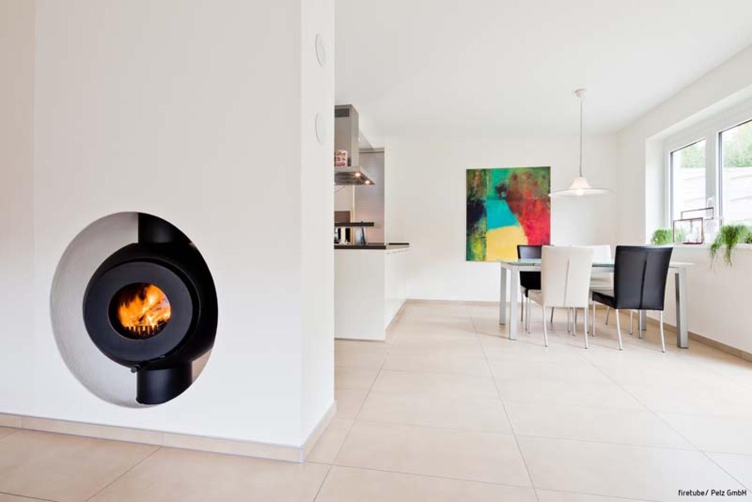 Schwarzer firetube Ofen mit sichtbarem Feuer, wandintegriert; im Hintergrund Wohn- und Essbereich.