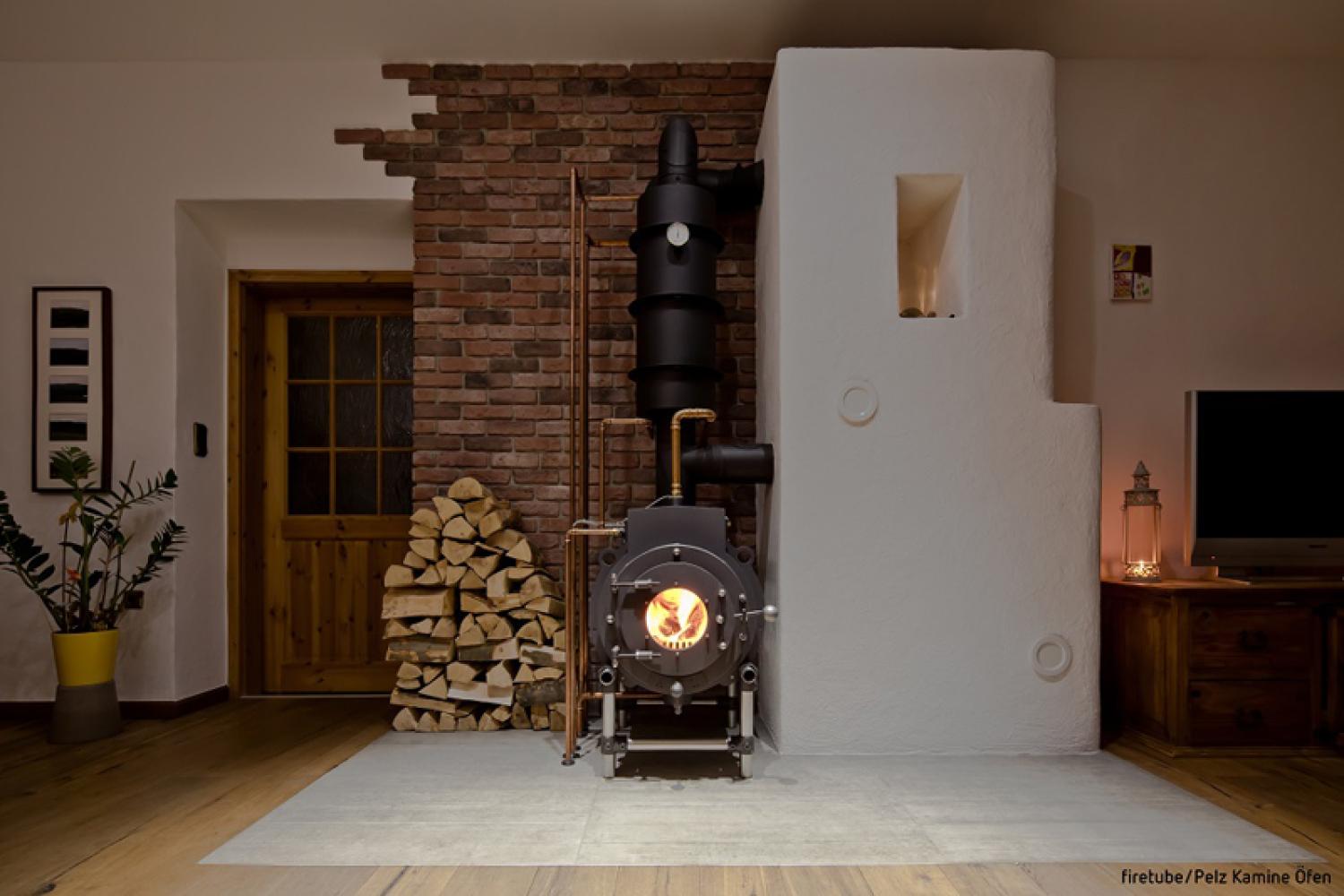 Schwarzer firetube Ofen mit sichtbarem Feuer in wohnlicher Atmosphäre; links daneben gestapelte Holzscheite.