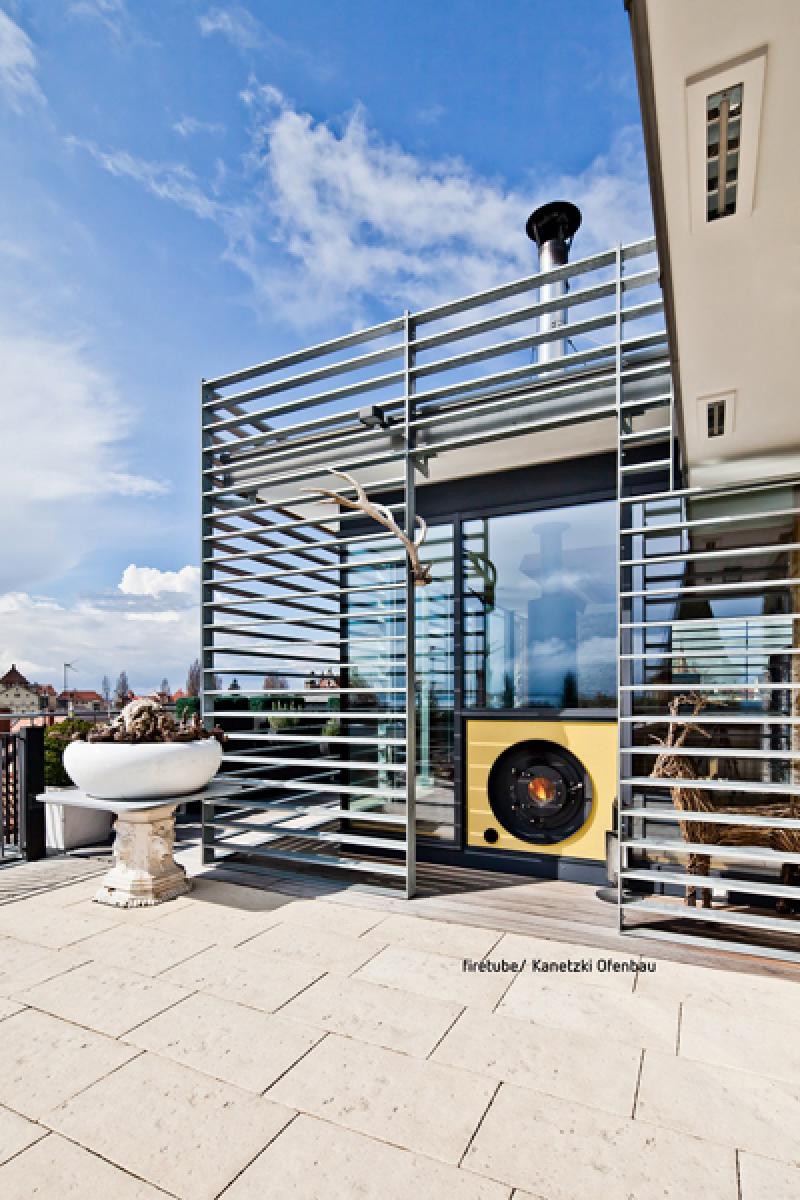 Moderne Terrasse mit firetube Ofen und sichtbarem Feuer, in die Glasfassade integriert.