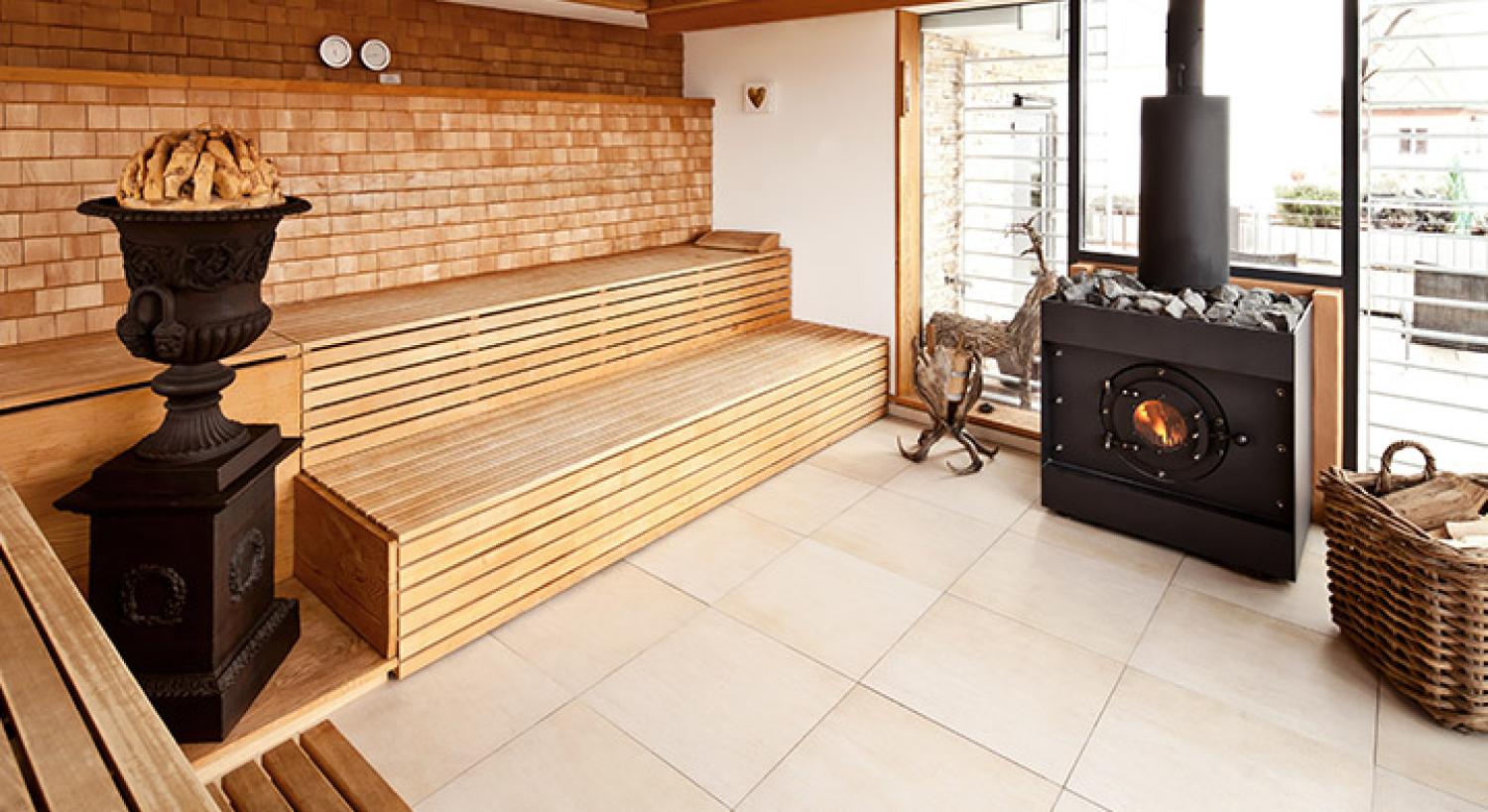 Firetube Saunaofen in einer Sauna mit Glaswand; daneben Holzdekoration, Korb mit Holzscheiten auf dem Boden und Sitzbänke aus Holz.