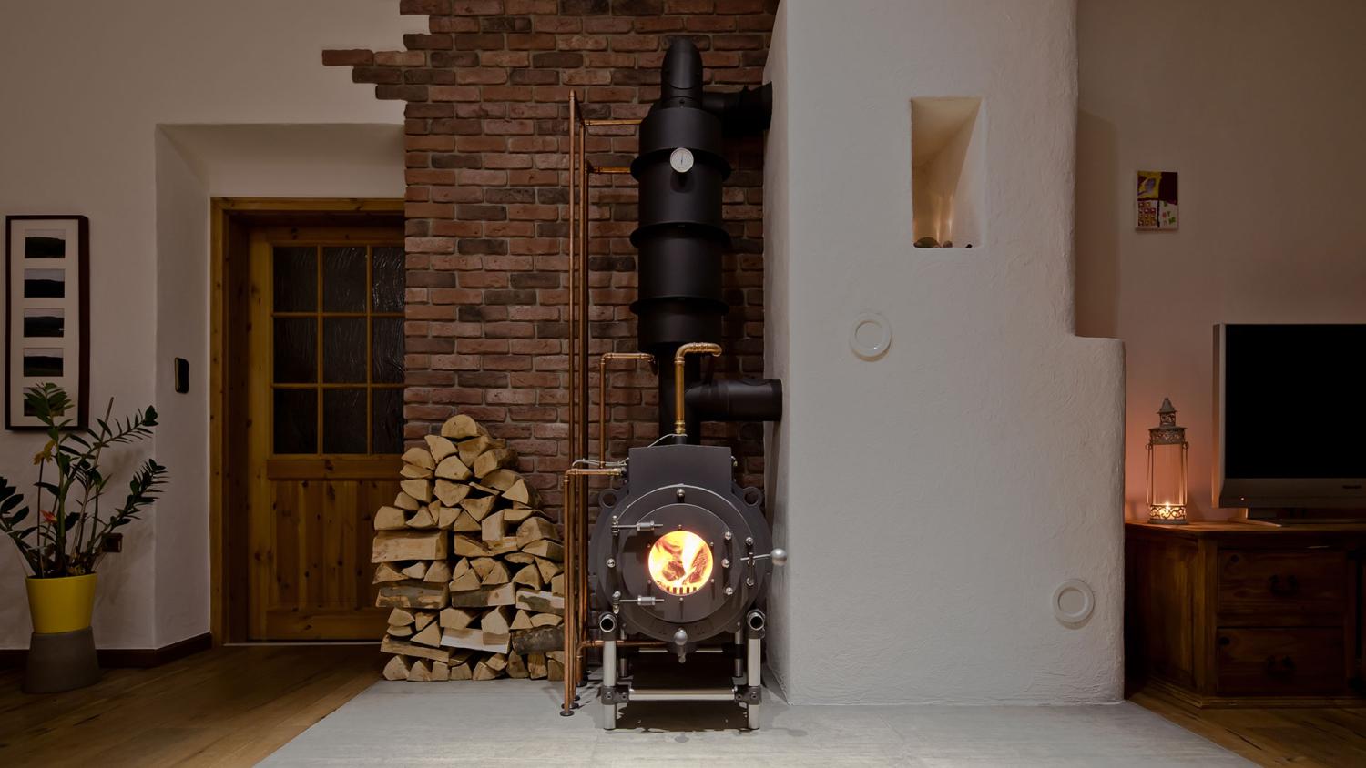Schwarzer firetube Ofen mit sichtbarem Feuer in wohnlicher Atmosphäre; links daneben gestapelte Holzscheite.