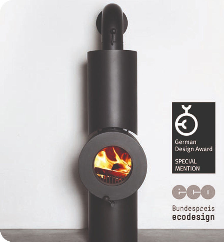 Schwarzer firetube Ofen mit sichtbarem Feuer vor weißer Wand; rechts Logos des German Design Award und des Bundespreis ecodesign.