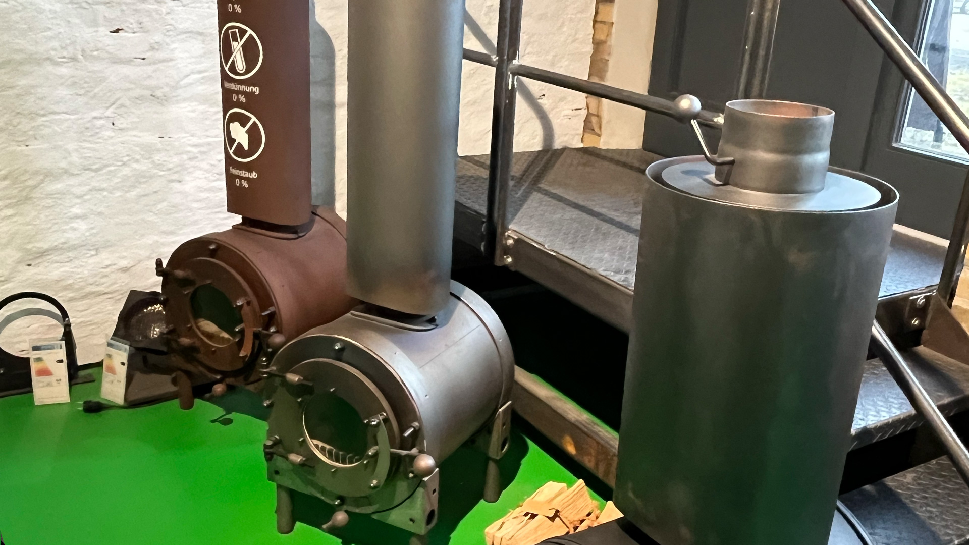 Zwei firetube Öfen nebeneinander in unterschiedlichen Ausführungen, vor einer weißen Wand und Treppen im Hintergrund.