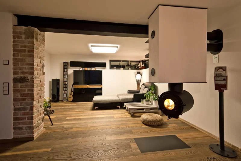 Modernes Wohnzimmer mit von der Decke hängendem schwarzen firetube Ofen und sichtbarem Feuer; im Hintergrund Möbel.